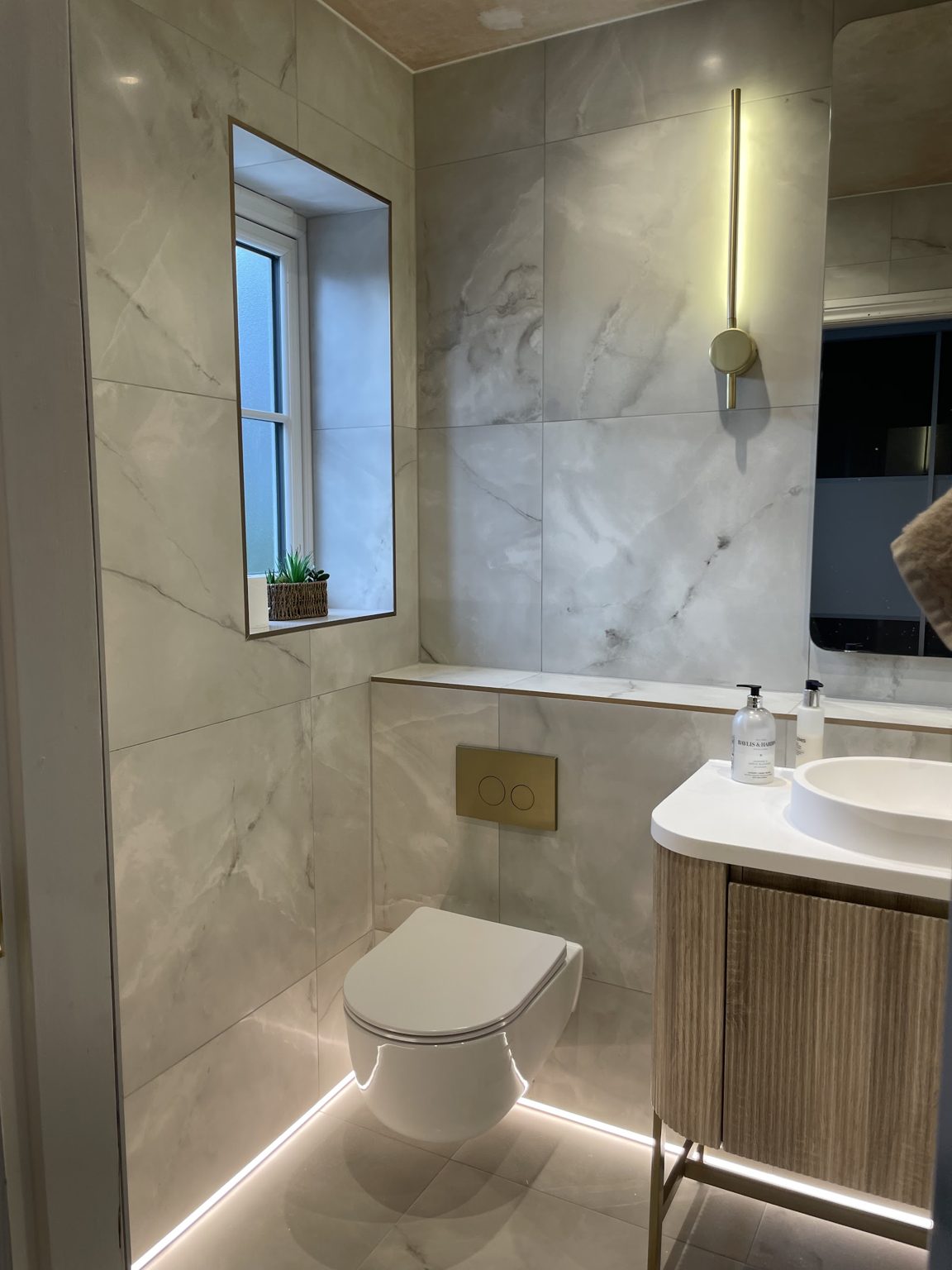Finished bathroom with low-level LED lighting and a brass wall light